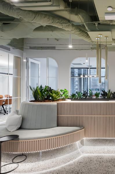 Modern office reception area with curved seating, indoor plants, glass partitions and soft lighting