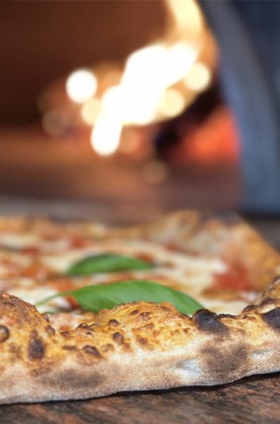 Close-up of wood-fired pizza cooking beside flames in a traditional oven
